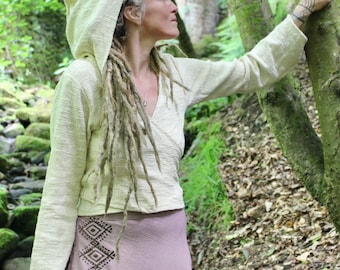 May include: A cream-colored long-sleeve wrap top with a hood and a textured fabric finish, paired with a mauve-colored skirt featuring a vertical row of dark brown geometric diamond patterns printed along the side of the garment.