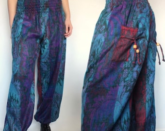 May include: Loose-fitting pants featuring a vibrant purple, blue, and black floral pattern. The garment has a high, elasticized smocked waistband, wide legs with gathered cuffs, and a side pocket accented with wooden beads on drawstrings.