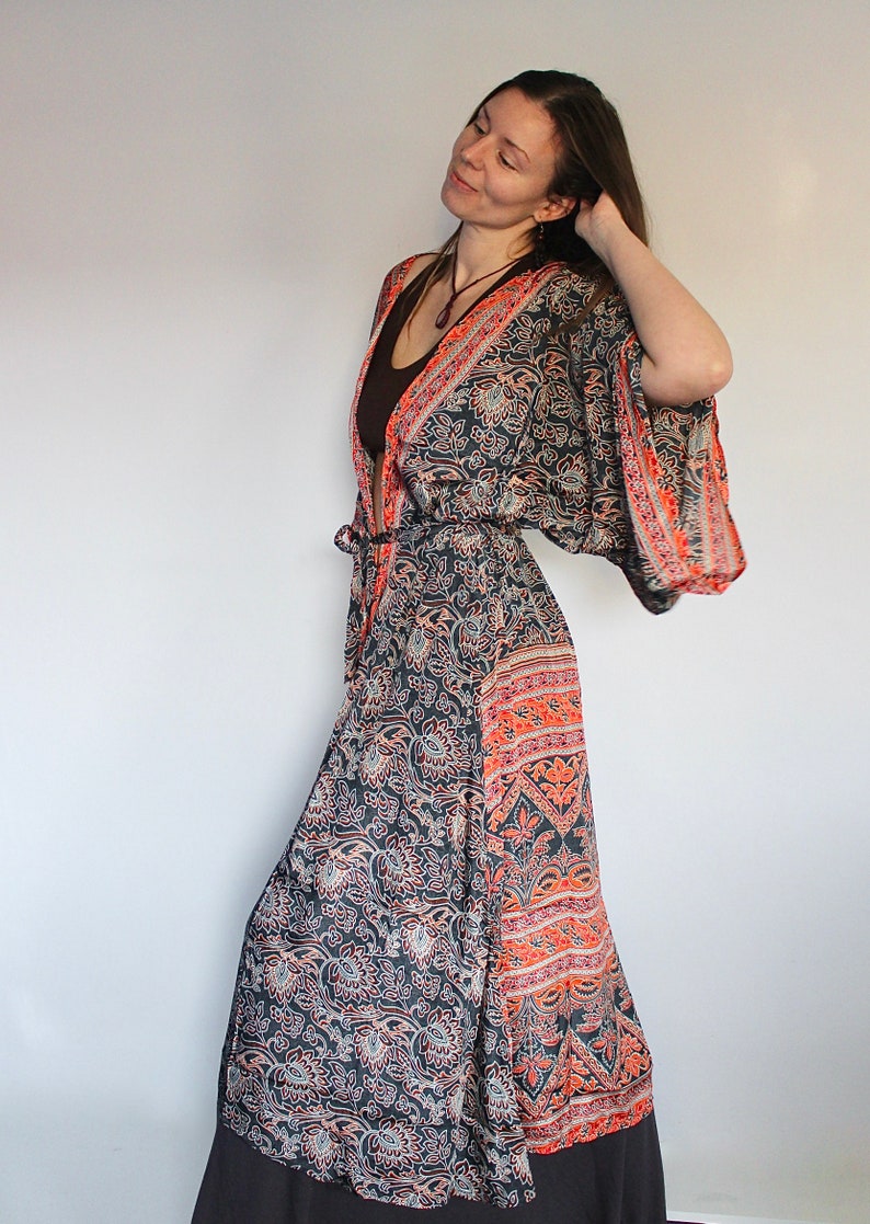 May include: A long, flowing black and orange patterned robe with a tie belt. The robe has a floral print and a wide, flowing sleeve.