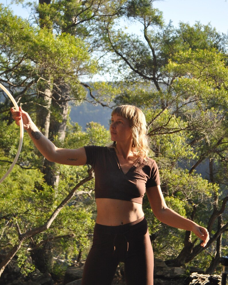May include: A dark brown short-sleeved V-neck crop top paired with matching dark brown leggings. The top features a fitted silhouette, while the leggings have a high-waisted design with a drawstring detail at the center of the waistband.