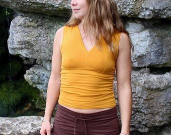May include: A mustard yellow sleeveless V-neck top with a fitted bodice and a subtle seam detail down the front, paired with dark brown pants featuring a drawstring waist and a smooth, solid-colored fabric construction.