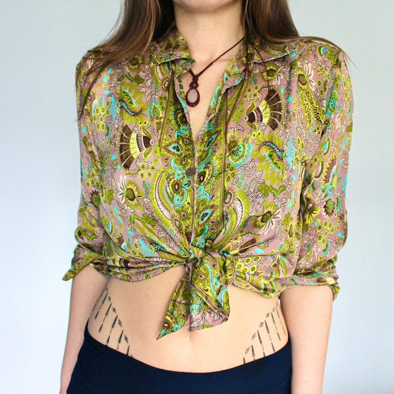 Op de afbeelding: Een lang mouw shirt met een paisley print in tinten van groen, bruin en roze. Het shirt is geknoopt in de taille en heeft een kraag.