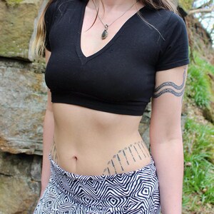 May include: A black short-sleeved crop top with a deep V-neckline paired with a skirt featuring a black and white geometric diamond pattern. The top is fitted and ends above the waist, while the skirt has a wide waistband and a repeating print.