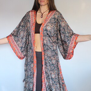 May include: A long, flowing black and orange patterned kimono with a floral design. The kimono has a wide, open neckline and long sleeves. The fabric is silky and soft.