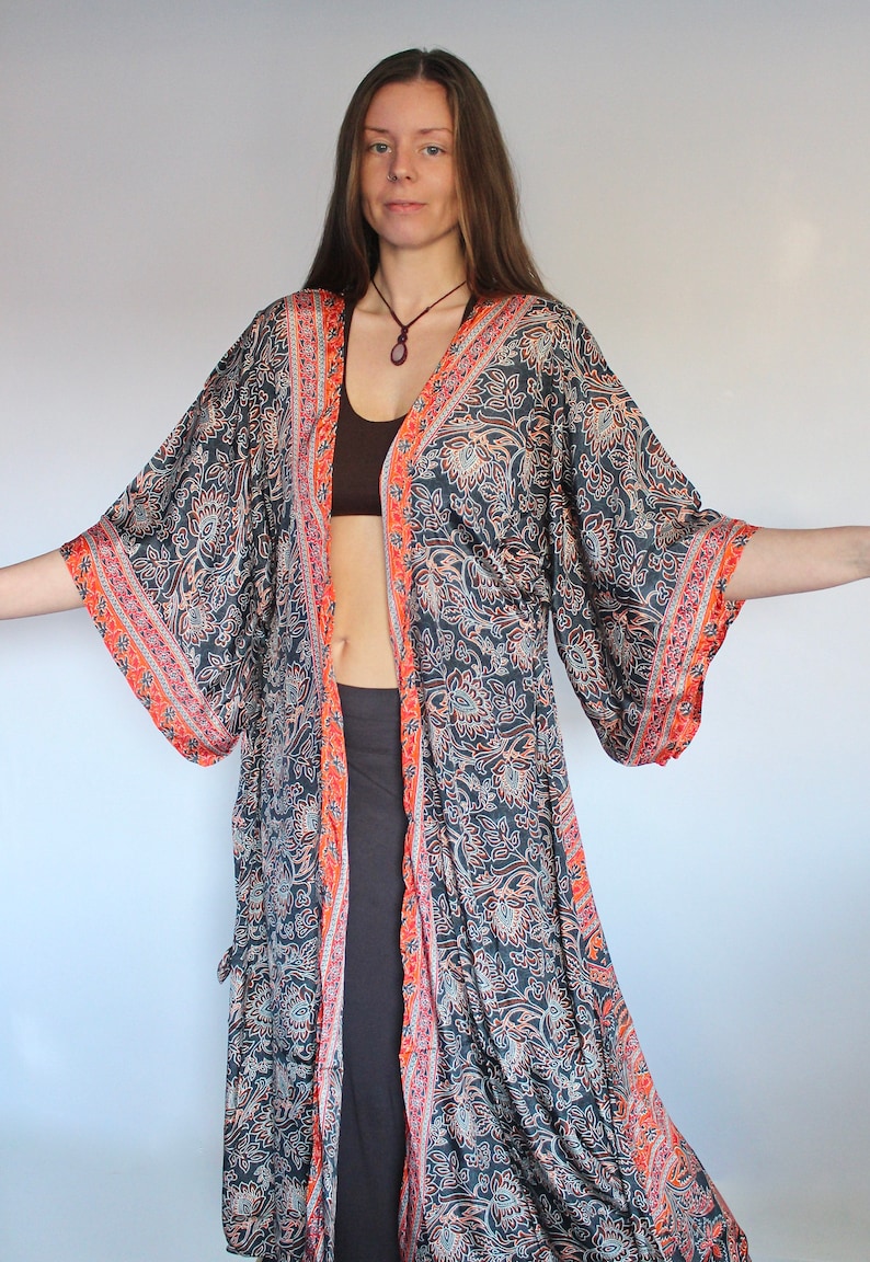 May include: A long, flowing black and orange patterned kimono with a floral design. The kimono has a wide, open neckline and long sleeves. The fabric is silky and soft.
