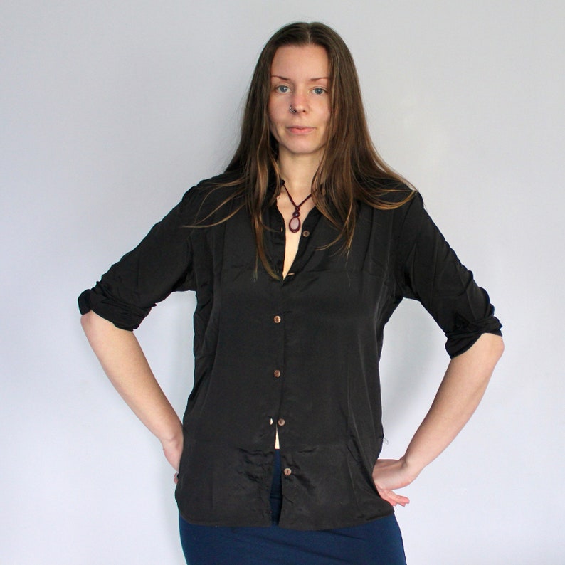 Puede incluir: Una mujer con una camisa negra de manga larga con botones y un collar con un colgante oscuro.