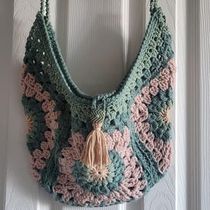 May include: A handmade crochet bag in a granny square pattern. The bag features a combination of soft green and pink hues, with a matching green strap. A tassel hangs from the center, adding a decorative touch to this unique accessory.