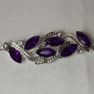 May include: A silver bracelet with a delicate design featuring multiple marquise-shaped purple gemstones. The bracelet has a clasp closure.