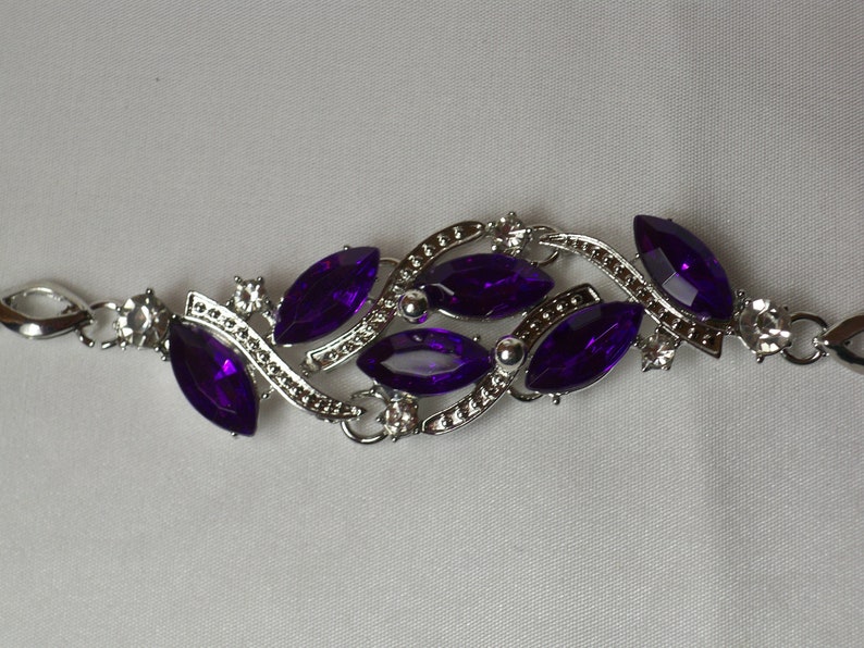 May include: A silver bracelet with a delicate design featuring multiple marquise-shaped purple gemstones. The bracelet has a clasp closure.