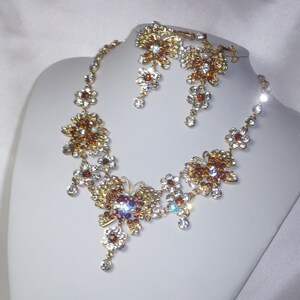 May include: A gold necklace and earrings set with clear and amber colored crystals in a butterfly design.