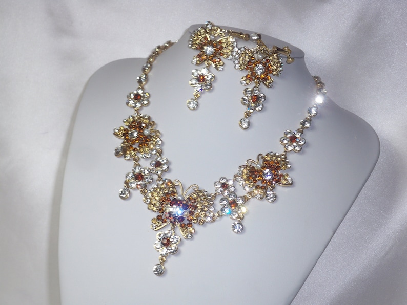 May include: A gold necklace and earrings set with clear and amber colored crystals in a butterfly design.
