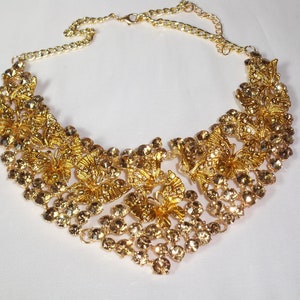 Puede incluir: Un collar dorado con dise&ntilde;os florales y de mariposas intrincados. El collar presenta numerosas piedras de estr&aacute;s redondas y transparentes y una delicada cadena para ajustar la longitud. El dise&ntilde;o es sim&eacute;trico y adecuado para ocasiones especiales.