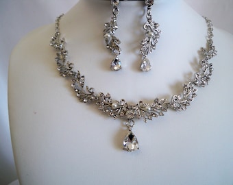 May include: A silver necklace and earrings set with a teardrop-shaped crystal pendant and leaf-shaped accents.