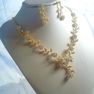 May include: A gold-toned necklace and earring set featuring a delicate vine motif with small clear crystals and white pearls. The necklace has a central floral cluster with teardrop-shaped crystals, while the earrings mirror the vine design.