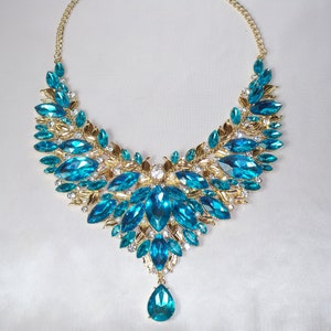 May include: A statement necklace featuring a gold-tone chain and setting. The necklace is adorned with large, vibrant blue-green gemstones and smaller clear crystals. A teardrop-shaped stone dangles from the center.
