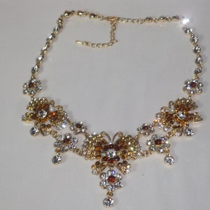 May include: A gold necklace with a butterfly pendant adorned with clear and amber rhinestones.