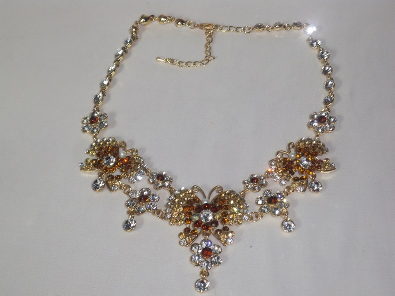 May include: A gold necklace with a butterfly pendant adorned with clear and amber rhinestones.