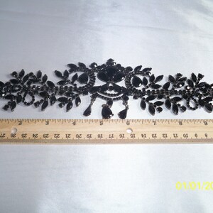 May include: Black rhinestone necklace with a floral design. The necklace features a central ornate design with dangling teardrop-shaped rhinestones. The necklace is approximately 10 inches long.