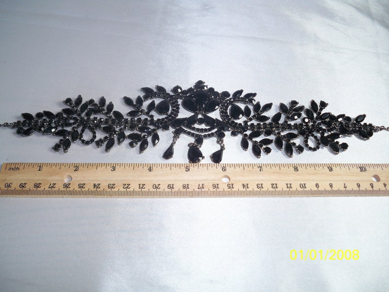 May include: Black rhinestone necklace with a floral design. The necklace features a central ornate design with dangling teardrop-shaped rhinestones. The necklace is approximately 10 inches long.