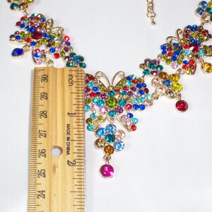 Puede incluir: Un collar de mariposa colorido con una cadena dorada y una variedad de piedras de cristal de colores. El collar mide aproximadamente 5 cm de largo.