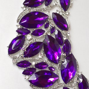 May include: A silver and purple jeweled necklace with a cascading design. The necklace is made of metal and features a variety of purple rhinestones in different sizes and shapes.