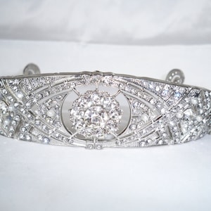 May include: A silver tiara with a large, clear rhinestone centerpiece and smaller rhinestones and pearls throughout.