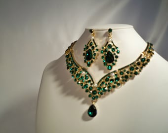 May include: A gold necklace and earrings set with emerald green and white stones. The necklace has a teardrop pendant.