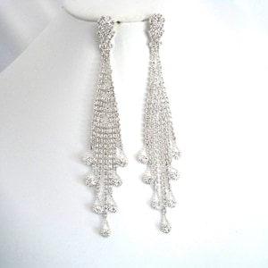 May include: A pair of long, silver dangle earrings with a cascade of clear rhinestones. The earrings are approximately 3 inches long.