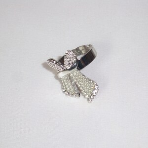 May include: Silver-toned ring featuring a bow design. The bow is adorned with small, clear rhinestones and faux pearls, with a white enamel accent. The ring is set against a white background.