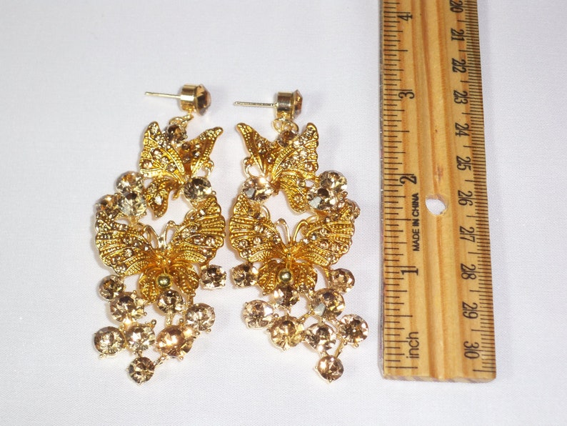 Puede incluir: Pendientes de mariposa dorados con pedrer&iacute;a transparente y color &aacute;mbar. Los pendientes tienen un dise&ntilde;o colgante con cierre de poste. Los pendientes miden aproximadamente 7.6 cm de largo.