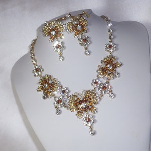 May include: A gold necklace and earrings set with clear and amber rhinestones. The necklace features a butterfly design with multiple crystal accents.