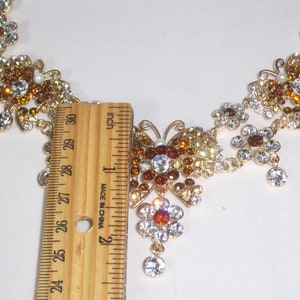May include: A gold necklace with a butterfly pendant. The butterfly is made of clear and amber rhinestones. The necklace is 18 inches long.