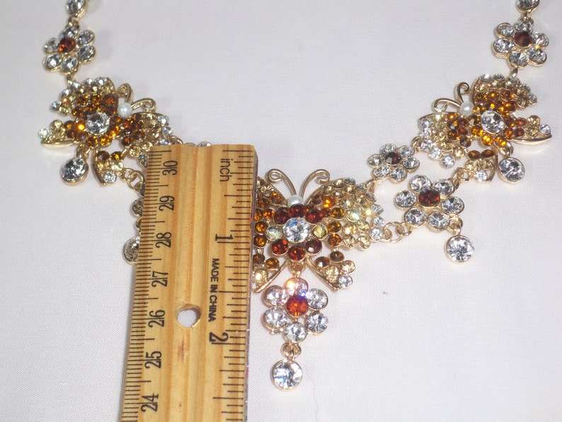 May include: A gold necklace with a butterfly pendant. The butterfly is made of clear and amber rhinestones. The necklace is 18 inches long.