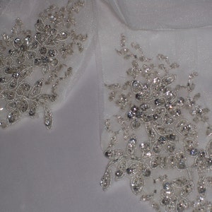 May include: Two white fabric embellishments with silver beading and floral designs.