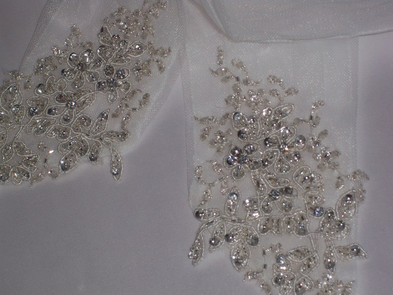 May include: Two white fabric embellishments with silver beading and floral designs.