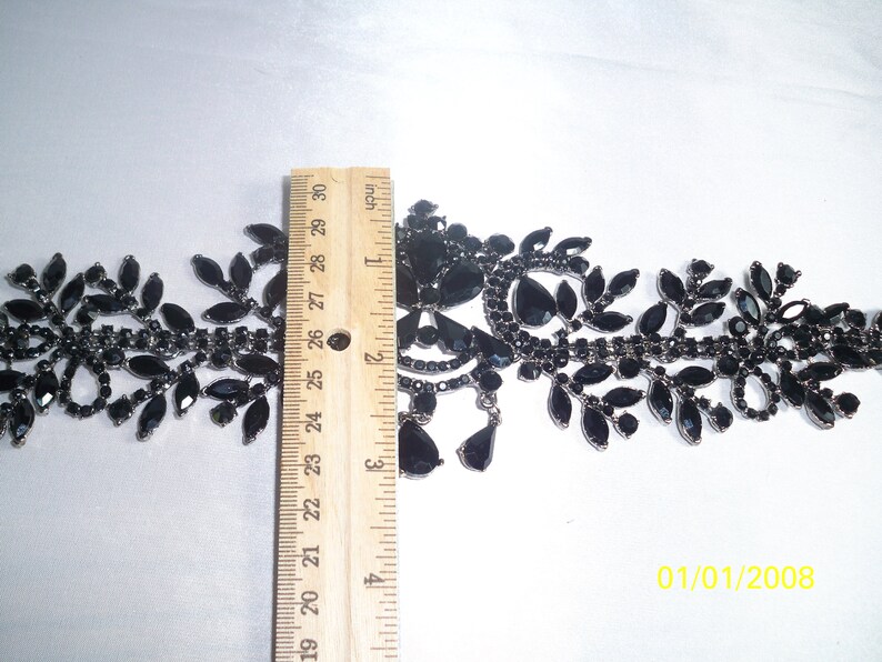 May include: Black rhinestone trim with leaf and teardrop designs. The trim is approximately 2 inches wide and is measured with a ruler. The trim is on a white background. The date 01/01/2008 is in the bottom right corner.