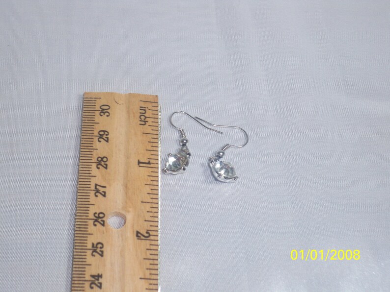 May include: A pair of silver earrings with clear crystal stones. The earrings are approximately 1 inch long.