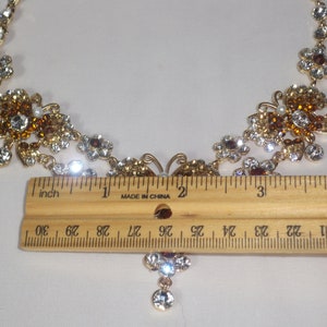 May include: A gold tone necklace with a butterfly pendant and clear and amber colored rhinestones. The necklace measures approximately 15 inches long.