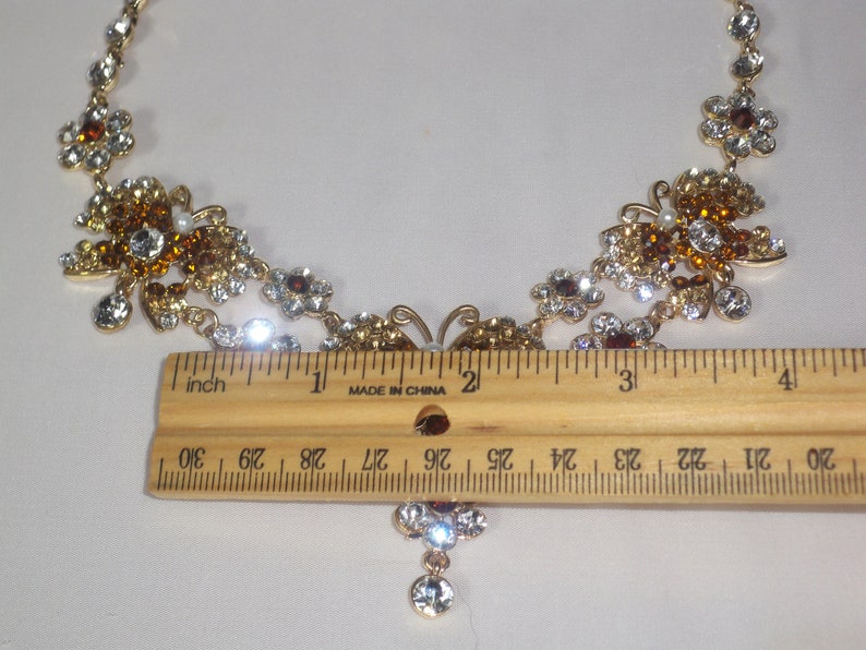 May include: A gold tone necklace with a butterfly pendant and clear and amber colored rhinestones. The necklace measures approximately 15 inches long.