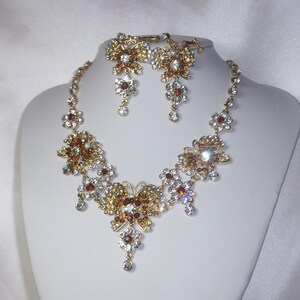 May include: A gold necklace and earrings set with clear and amber-colored crystals in a butterfly design.