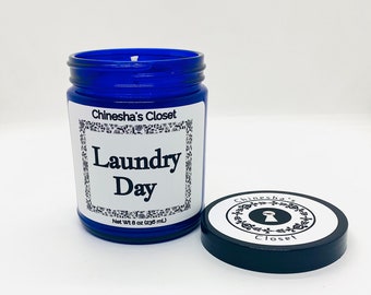 May include: A blue glass jar candle with a white label that reads "Chinesha's Closet Laundry Day" and "Net Wt 8 oz (236 mL)". The candle has a black lid with a white label that reads "Chinesha's Closet" with a keyhole graphic.