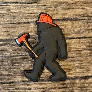 May include: A black rubber patch depicting a Bigfoot wearing a red firefighter helmet and holding an axe.
