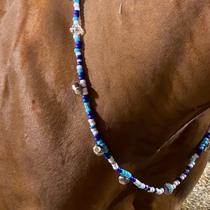 May include: A blue, white, and turquoise beaded horse necklace with silver bells and a crystal charm.