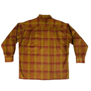 Op de afbeelding: Een lang mouw overhemd met knopen en een geruit patroon in tinten bruin, oranje en rood.
