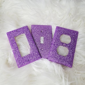 May include: Three purple glitter light switch and outlet covers. The covers are made of a sparkly material and have a textured finish.