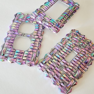 May include: Three iridescent purple and pink crystal outlet covers. The covers are made of small, faceted crystals that create a shimmering effect.