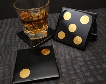 May include: Four black square coasters with gold polka dots. One coaster has a glass of amber liquid on top.
