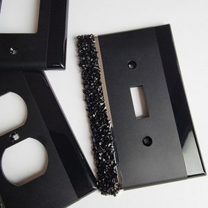 May include: Three black light switch covers with a decorative black and silver trim. The switch covers have a single toggle switch and a single outlet.
