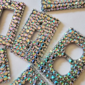 May include: A set of decorative light switch covers with iridescent rhinestones. The covers are made of a silver-toned metal base and feature a variety of sizes and shapes of rhinestones.