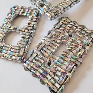 May include: Three iridescent light switch covers made of small, faceted glass tiles. The covers are in a geometric pattern and have a sparkly, glittery appearance.